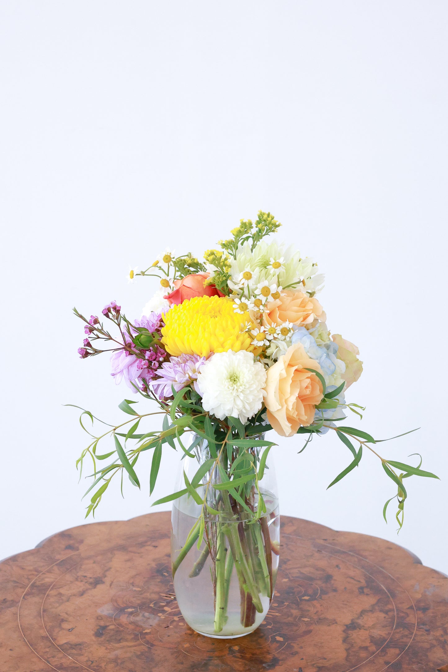 Bouquet of colorful flowers in a clear vase on a wooden surface with a light gray background